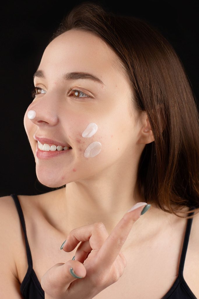 Woman applying facial cream with clear, even skin