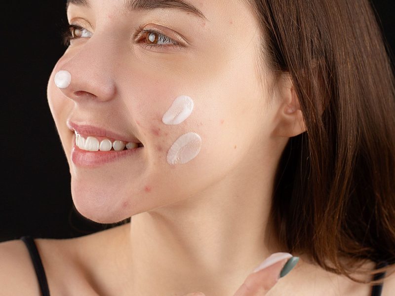 Woman applying facial cream with clear, even skin